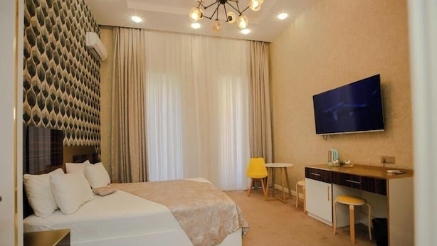 A hotel room with a bed, a desk, a chair, a TV, and a window with curtains. - Dionis Hotel (Baku)