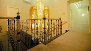 A grand staircase with ornate balustrades leading to a landing with a chandelier. - Dionis Hotel (Baku)