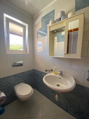 A bathroom with a toilet, sink, and window. - Apartment Niko (Novi Vinodolski)