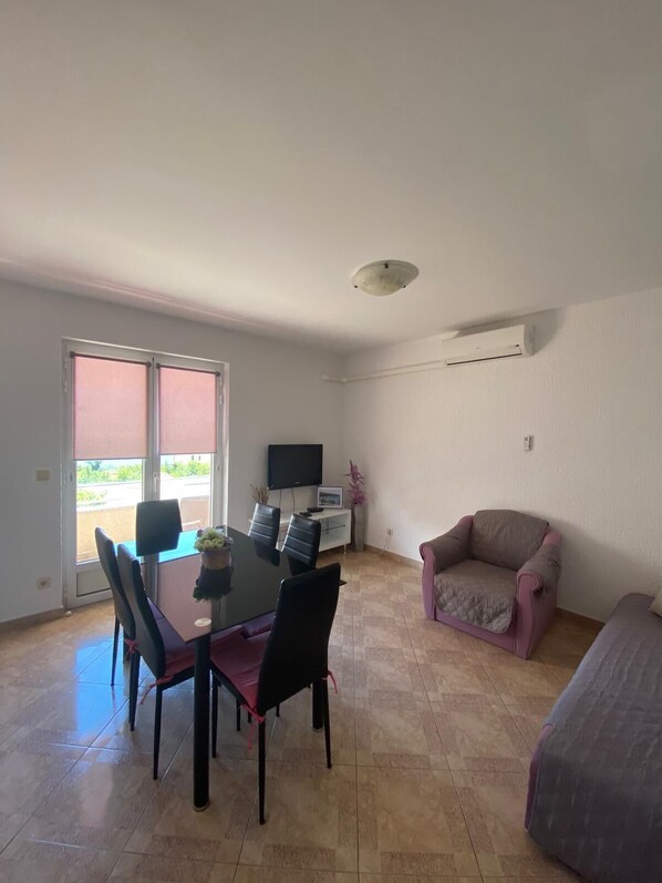 A dining area with a table and chairs, a sofa, a TV, and an air conditioning unit. - Apartment Niko (Novi Vinodolski)