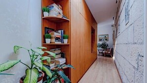 Kapea käytävä, jonka seinustalla on puinen kirjahylly täynnä kirjoja ja ruukkukasveja, johtaa huoneeseen, jonka seinällä on taulu.