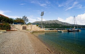 A pebbled beach with boats, a stone wall, and a mountain in the background. - Apartment Touch (Korčula)