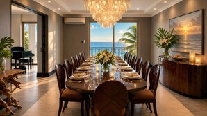 Een eetzaal met een grote gedekte tafel, een weelderige kroonluchter en uitzicht op de oceaan.