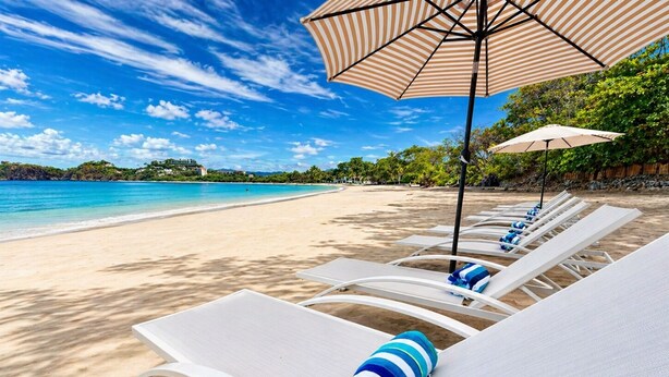 Een strand met witte ligstoelen en gestreepte parasols.
