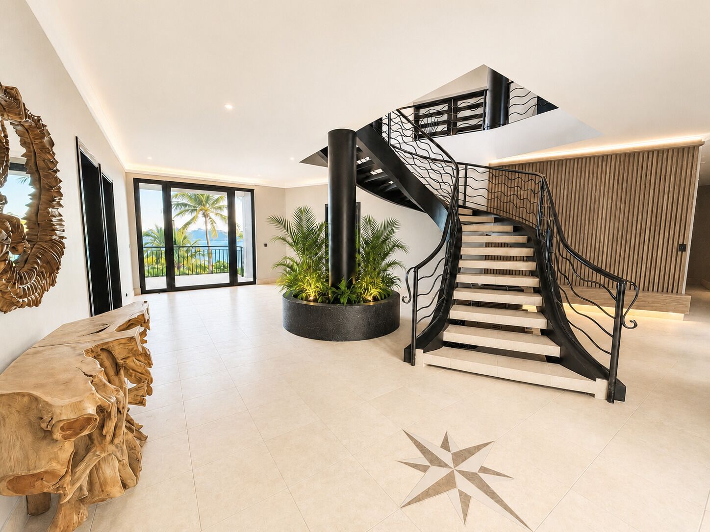 Un intérieur moderne avec un escalier en colimaçon, une grande table en bois et un sol orné d’un motif en étoile.