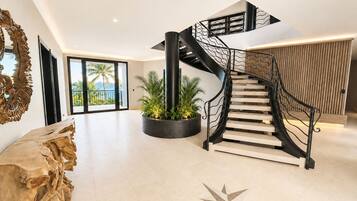 Un intérieur moderne avec un escalier en colimaçon, une grande table en bois et un sol orné d’un motif en étoile.