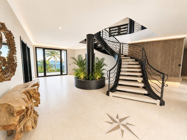 Un intérieur moderne avec un escalier en colimaçon, une grande table en bois et un sol orné d’un motif en étoile.