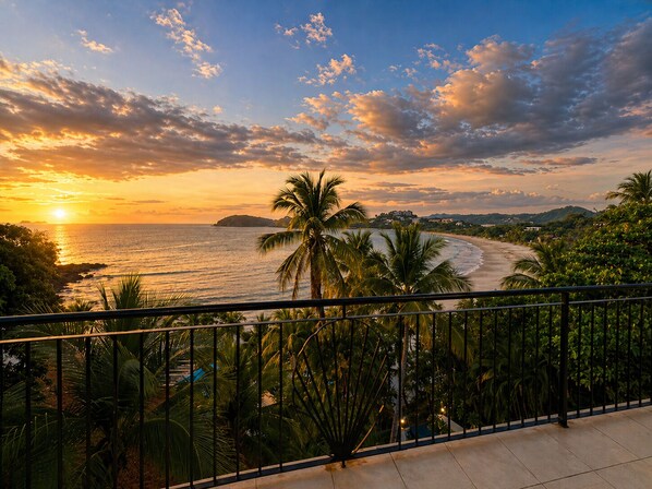 A balcony with a view of a beach and ocean during sunset.