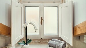 Un baño con tragaluz, vigas de madera, un lavabo blanco, una planta en maceta, toallas y una zona de ducha.