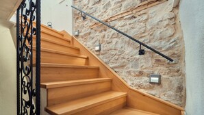 Una escalera de madera con un muro de piedra de fondo y barandillas metálicas.
