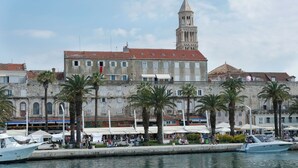 Un puerto deportivo con barcos amarrados, un edificio histórico con torre y palmeras bordeando el muelle.