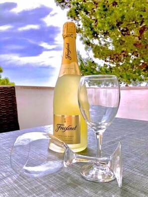 A bottle of Freixenet champagne and a wine glass on an outdoor table with a view of trees and sky. - Apartments Secret Beach (Omis)