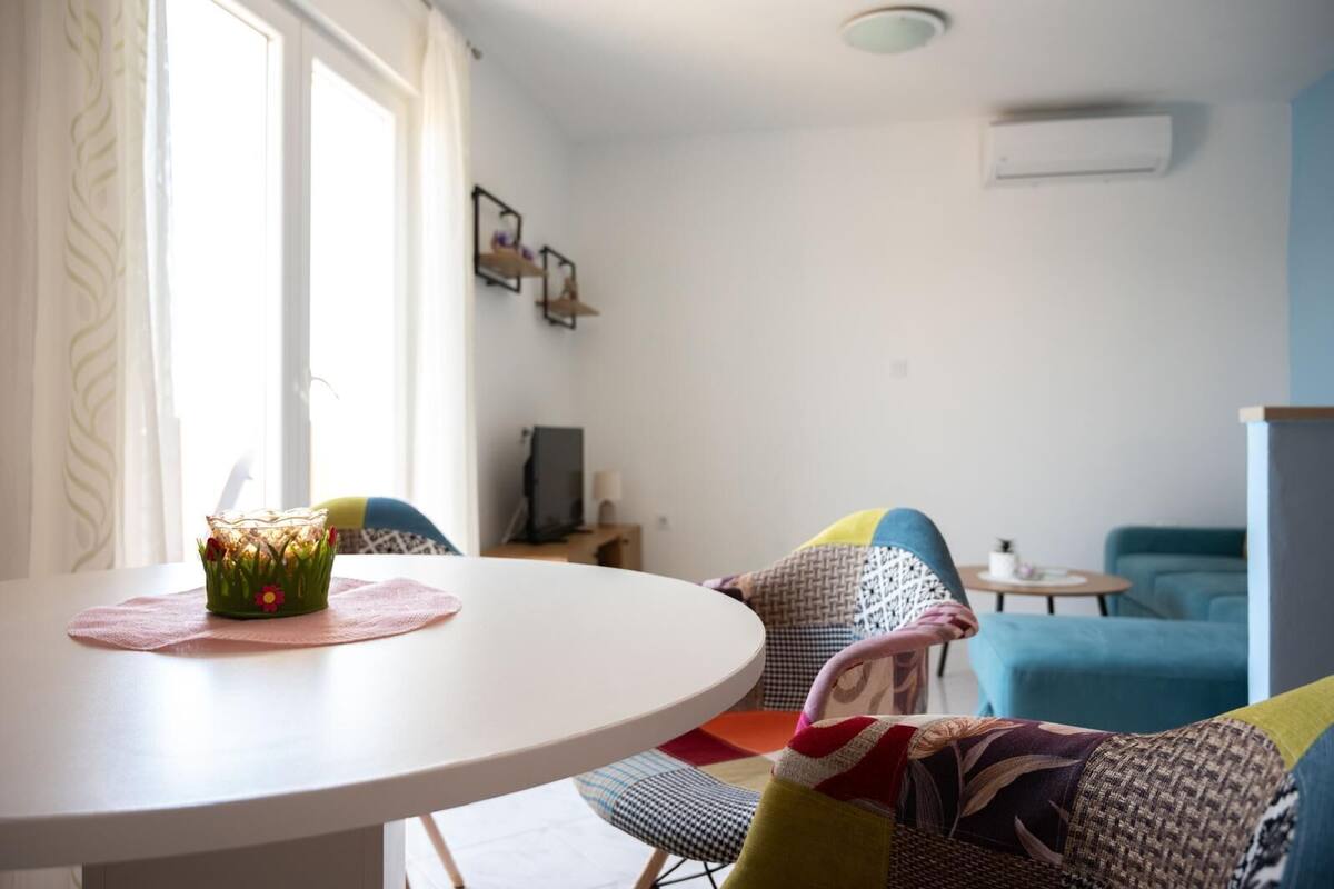 Un salon moderne avec une table ronde blanche, des chaises colorées et un téléviseur posé sur un meuble.