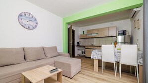 A modern living room with a beige sofa, a wooden coffee table, and a kitchen area with wooden cabinets and a dining table with white chairs. - Apartments Ante (Senj)