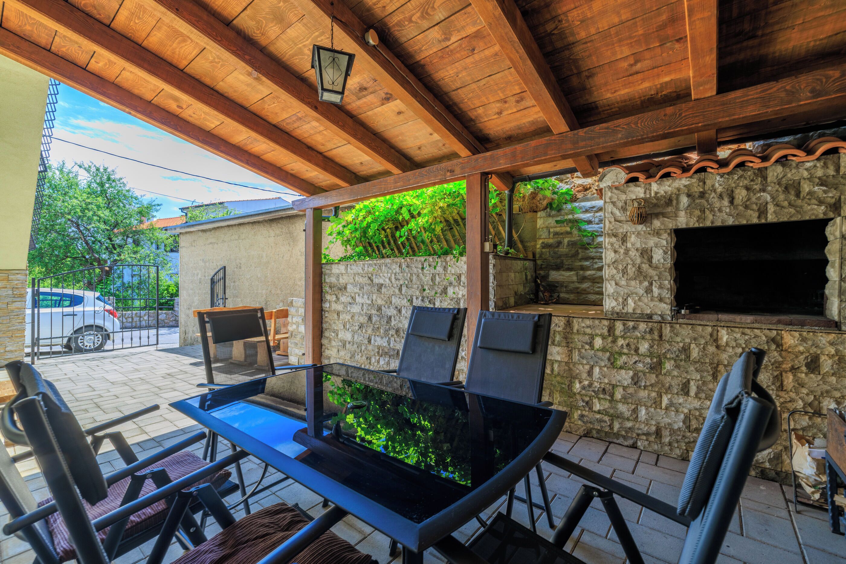 Un patio al aire libre con una mesa de vidrio, sillas y un muro de piedra.