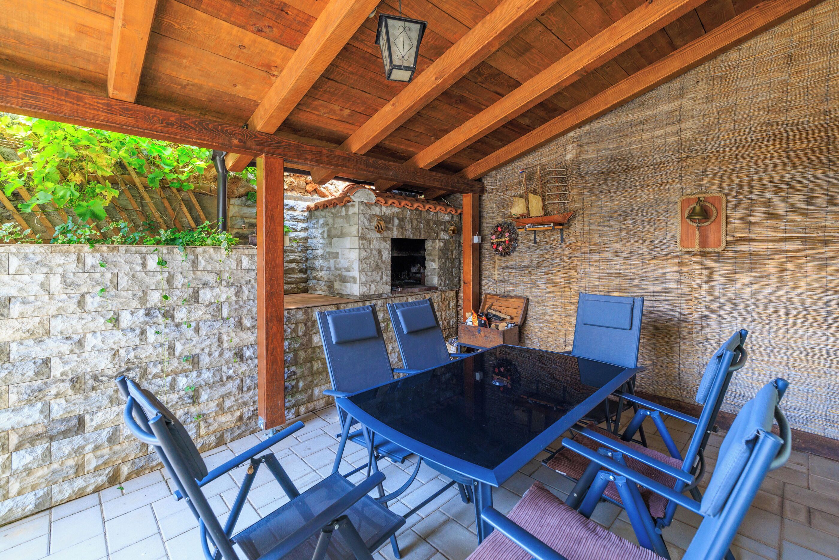 An outdoor patio with a stone wall, a wooden ceiling, and a stone fireplace.