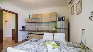 A compact kitchen with wooden cabinets, a refrigerator, and a dining area with a table set for two. - Apartments Ante (Senj)