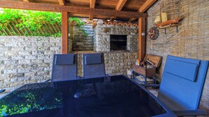 A stone fireplace with a chimney, a black table, and a blue chair in a covered outdoor area. - Apartments Ante (Senj)