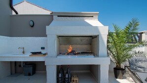 Una cocina exterior con una parrilla empotrada, un fregadero y un cubo de basura.
