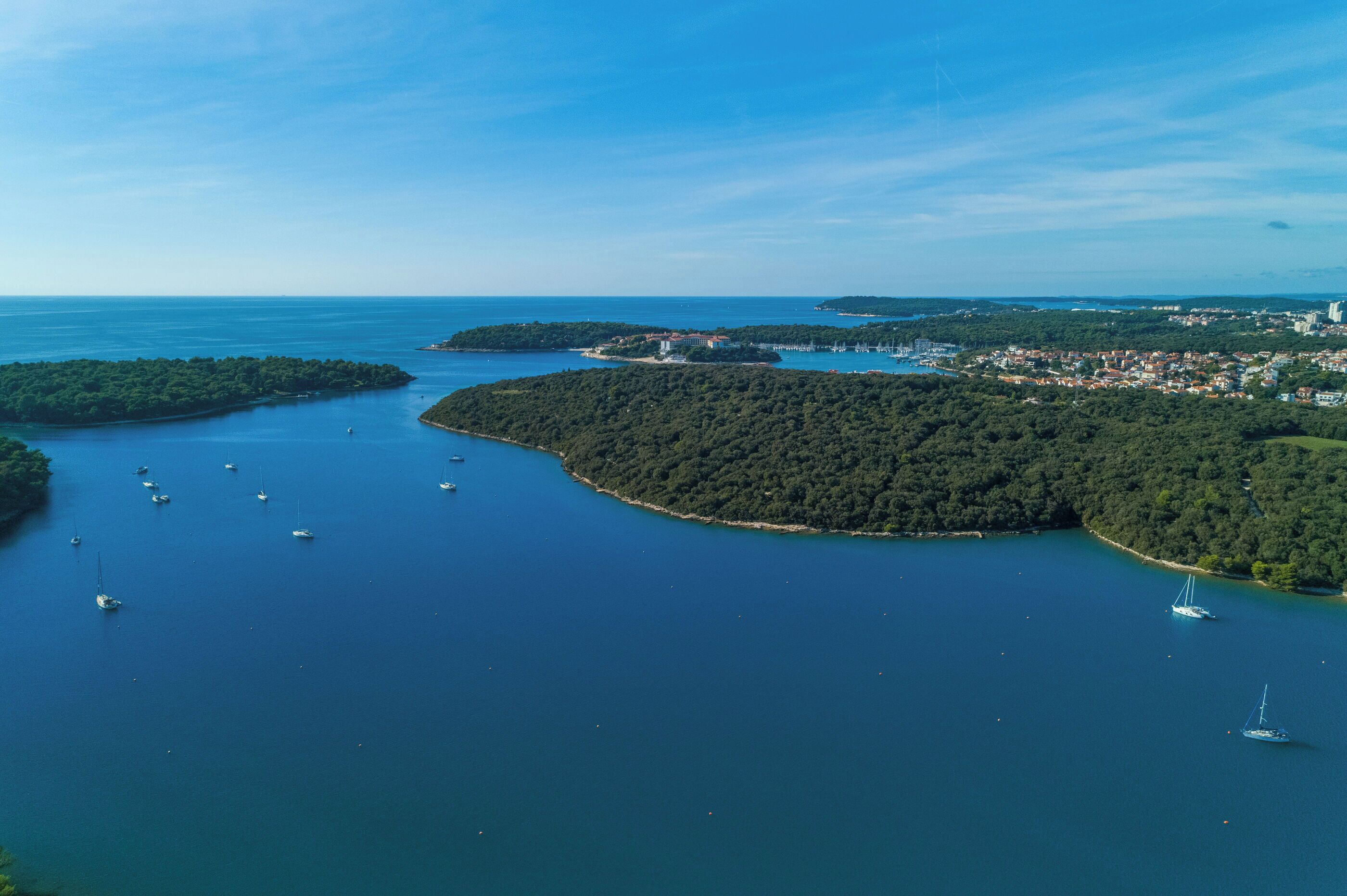 An aerial view of a coastal area with multiple islands, clear blue waters, and several boats.