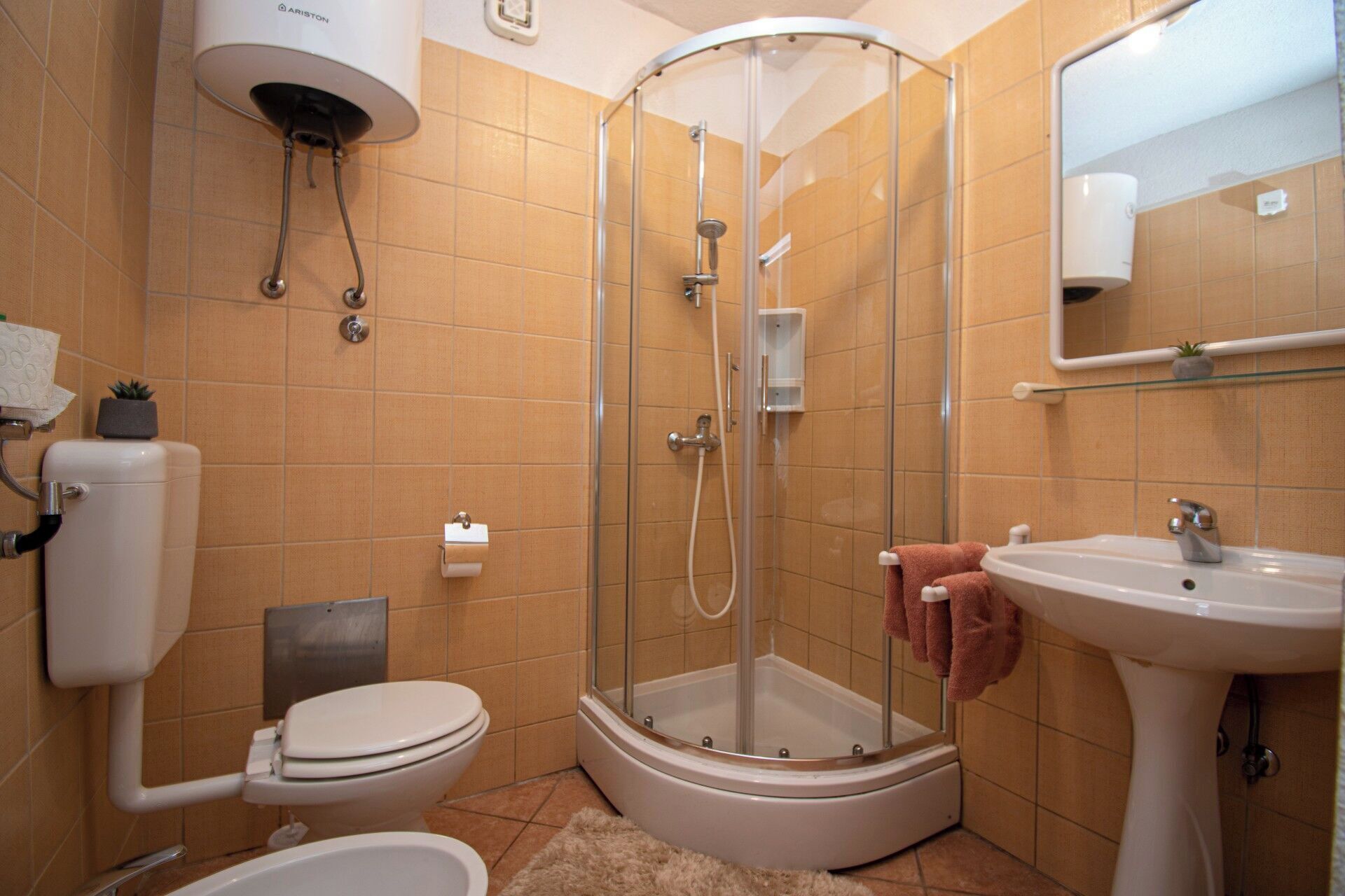 A bathroom with a shower, toilet, sink, and a mirror.