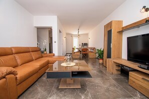 Una sala de estar moderna con un sofá de cuero, una mesa de centro de vidrio, un comedor con una mesa y sillas de madera, y un televisor de pantalla plana montado sobre un mueble de madera.
