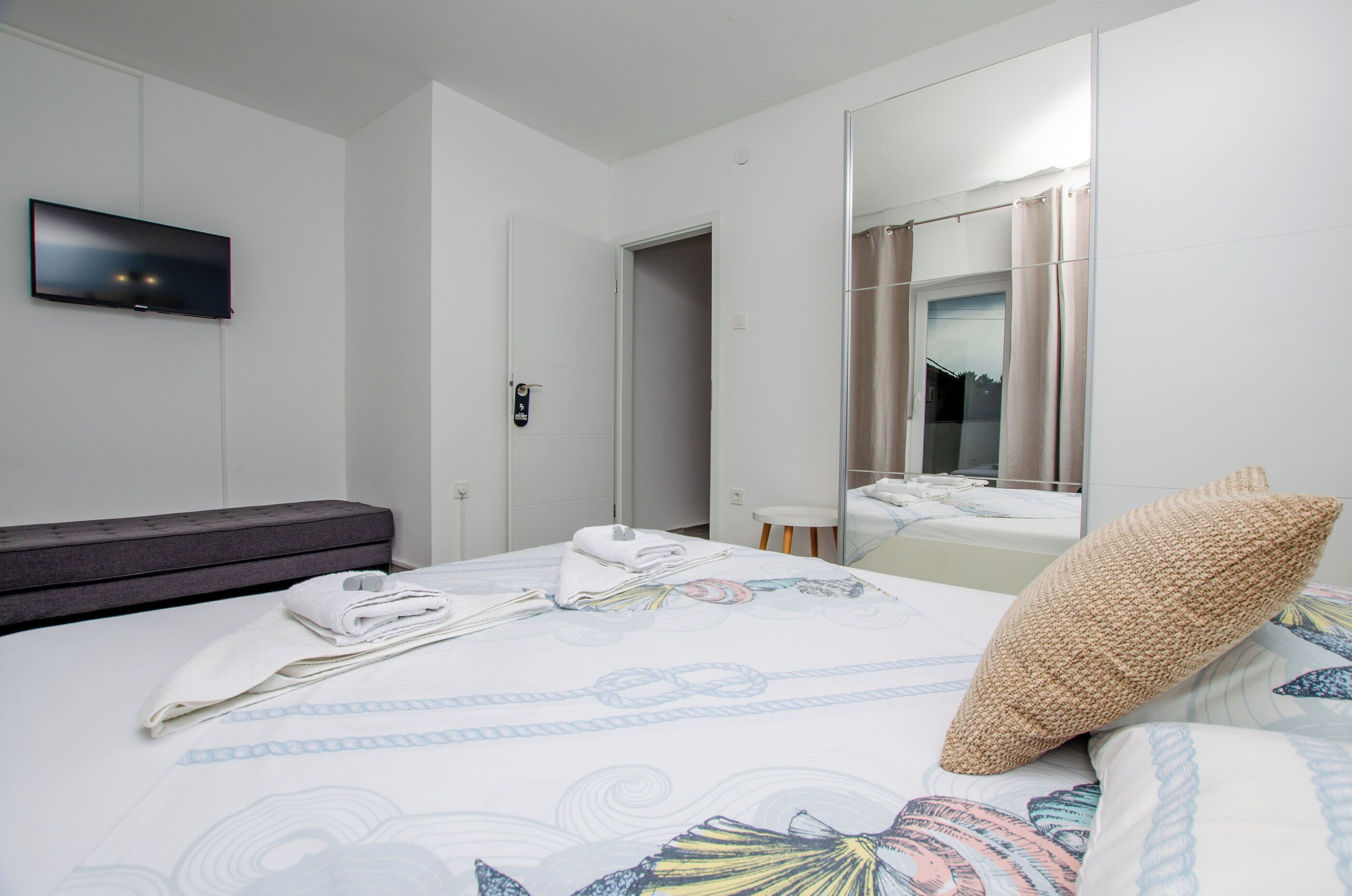 Une chambre d’hôtel avec un lit, un téléviseur à écran plat fixé au mur, une porte et un miroir qui reflète la salle de bain.