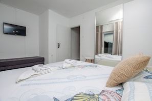 Une chambre d’hôtel avec un lit, un téléviseur à écran plat fixé au mur, une porte et un miroir qui reflète la salle de bain.