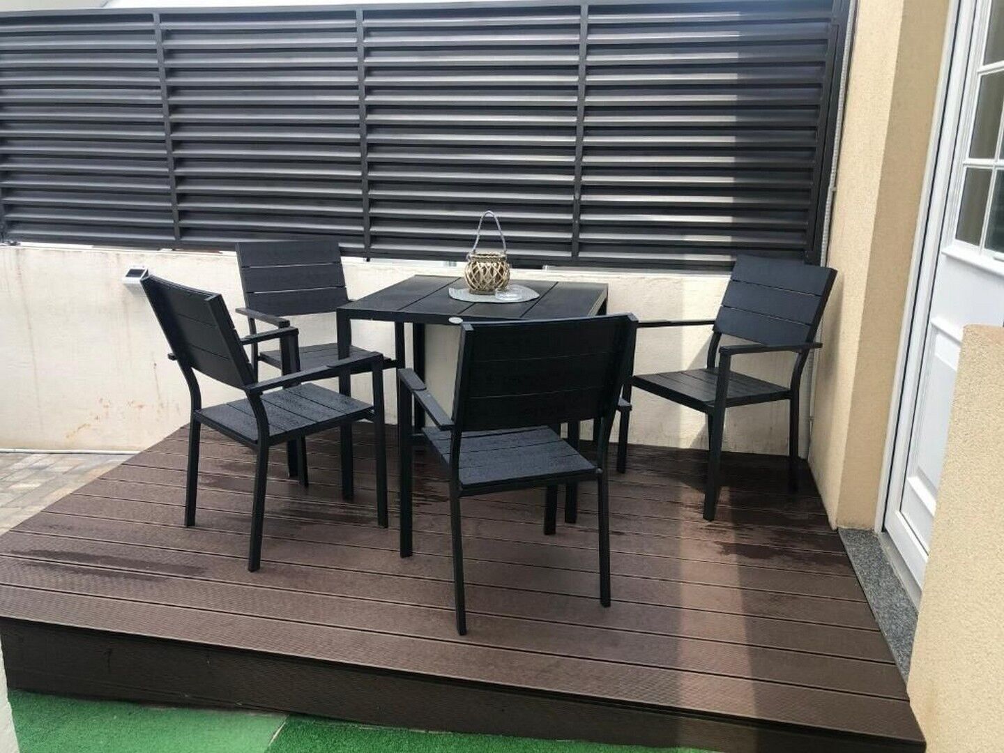Eine Außenpatio mit Tisch und vier Stühlen, einem dekorativen Gegenstand auf dem Tisch und einem Fenster mit Jalousien.
