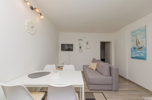 Un salon moderne avec une table blanche, un canapé gris et un tableau représentant des voiliers accroché au mur.