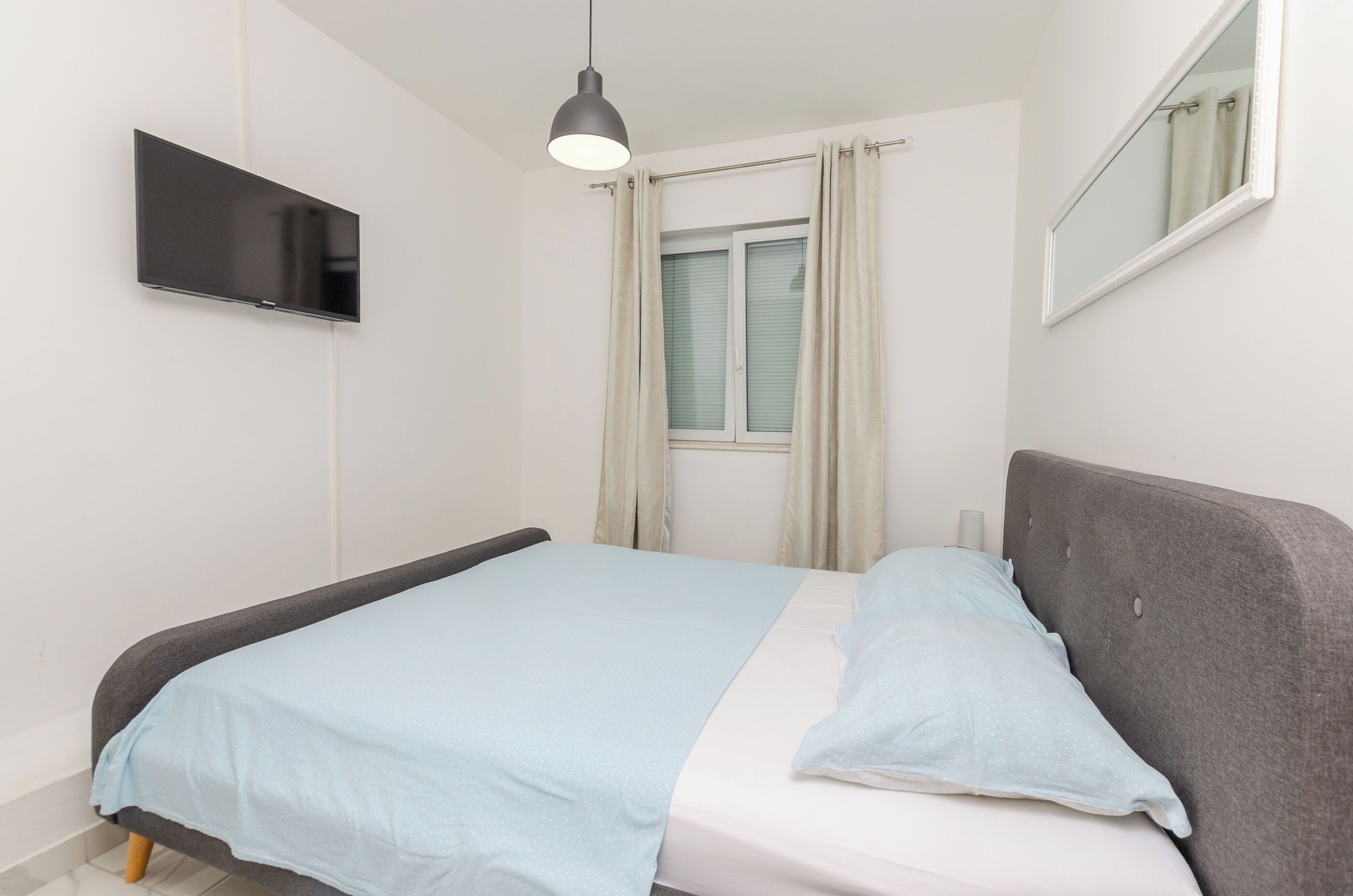 Une chambre à coucher comprenant un lit, un téléviseur à écran plat fixé au mur, une fenêtre avec des rideaux et un miroir sur le mur.