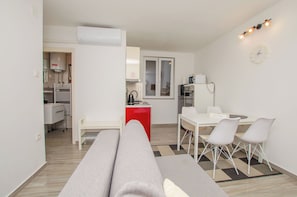 Un salon moderne avec un canapé, un coin repas comprenant une table et des chaises, une cuisine avec un meuble rouge et une horloge au mur.