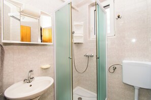 A bathroom with a sink, mirror, shower, and toilet. - Apartments Krunoslava (Vodice)