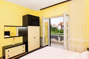 Une chambre à coucher comprenant un lit, une commode, un miroir et une porte-fenêtre coulissante donnant sur un balcon.