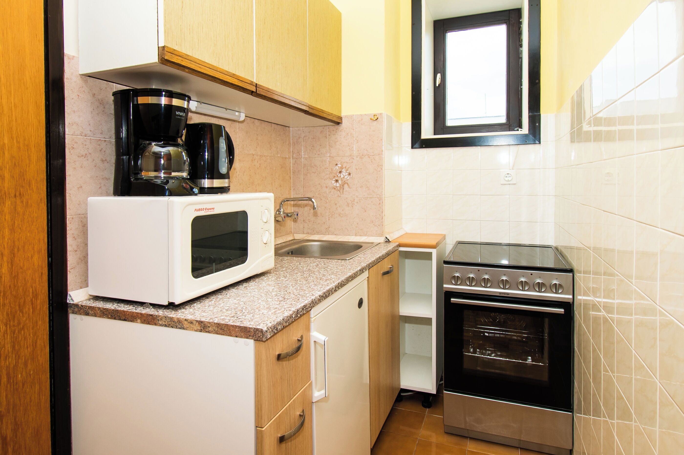 A compact kitchen with a microwave, coffee maker, sink, and oven.