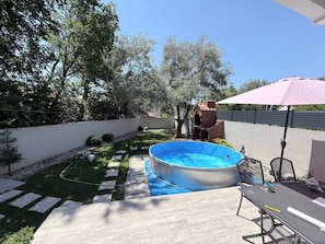 A backyard with a swimming pool, a brick structure, and a patio table with an umbrella. - Villa Mungo (Starigrad)