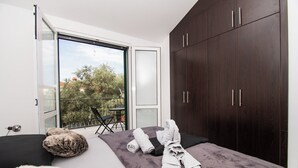 A modern bedroom with a large bed, dark wooden wardrobe, and a balcony with a table and chairs. - Villa Mungo (Starigrad)