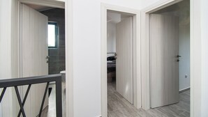 A hallway with white doors leading to a bedroom with a bed and a bathroom with a toilet and a shower. - Villa Mungo (Starigrad)