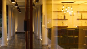 Un couloir bordé de colonnes, un espace bar avec des étagères et des luminaires suspendus.