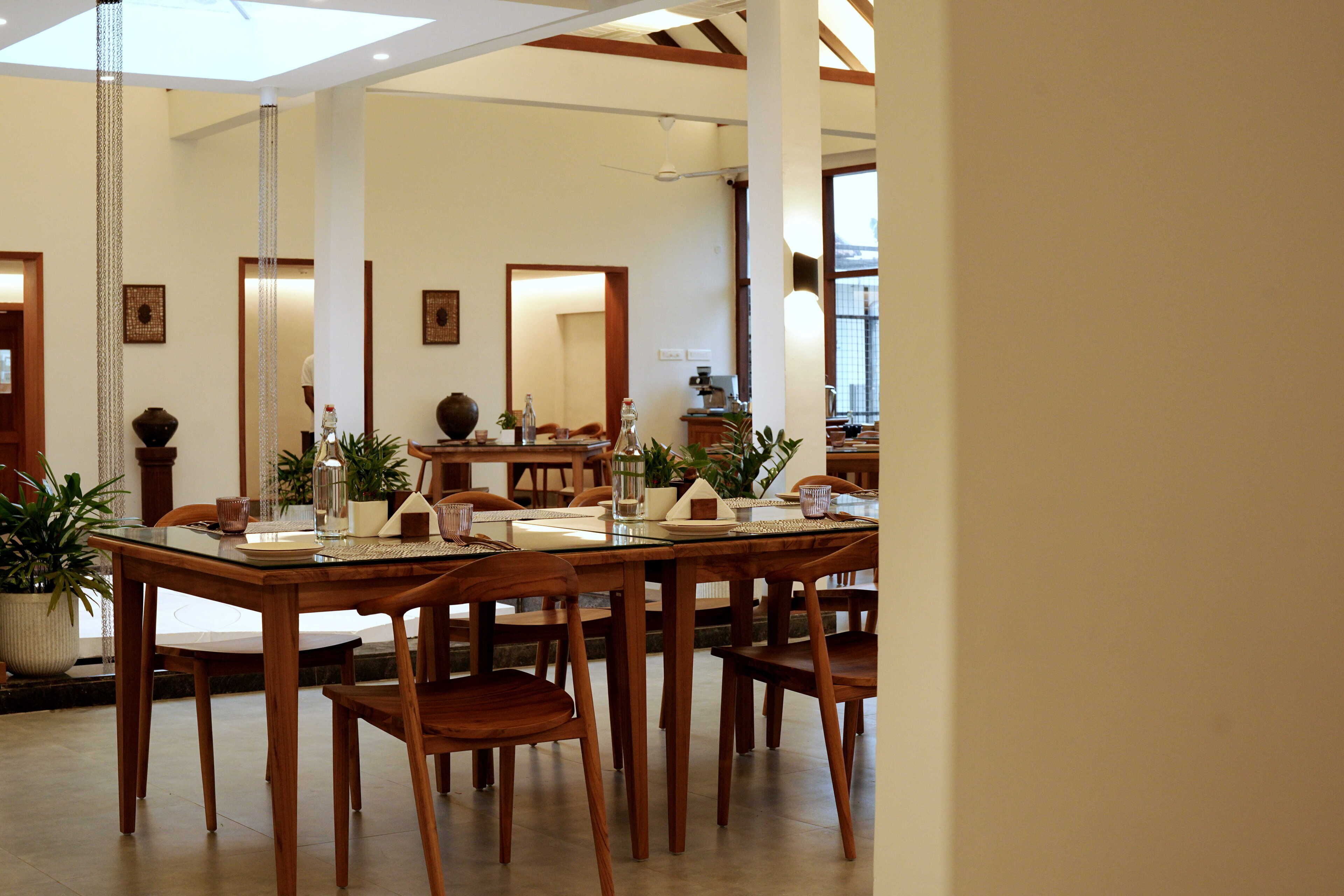 A spacious dining area with a high ceiling, wooden furniture, and large windows allowing natural light.