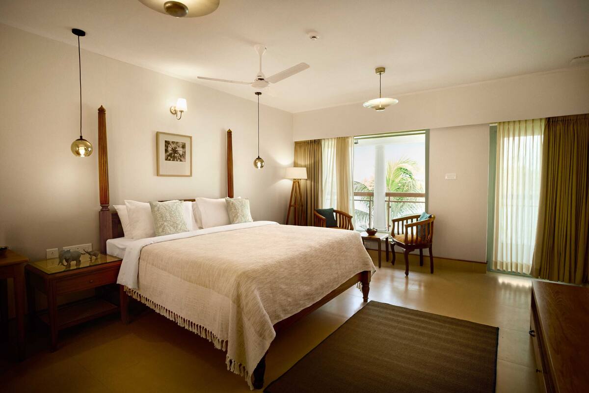Habitación de hotel con una cama grande, un escritorio con silla, un ventilador de techo y una ventana con cortinas.