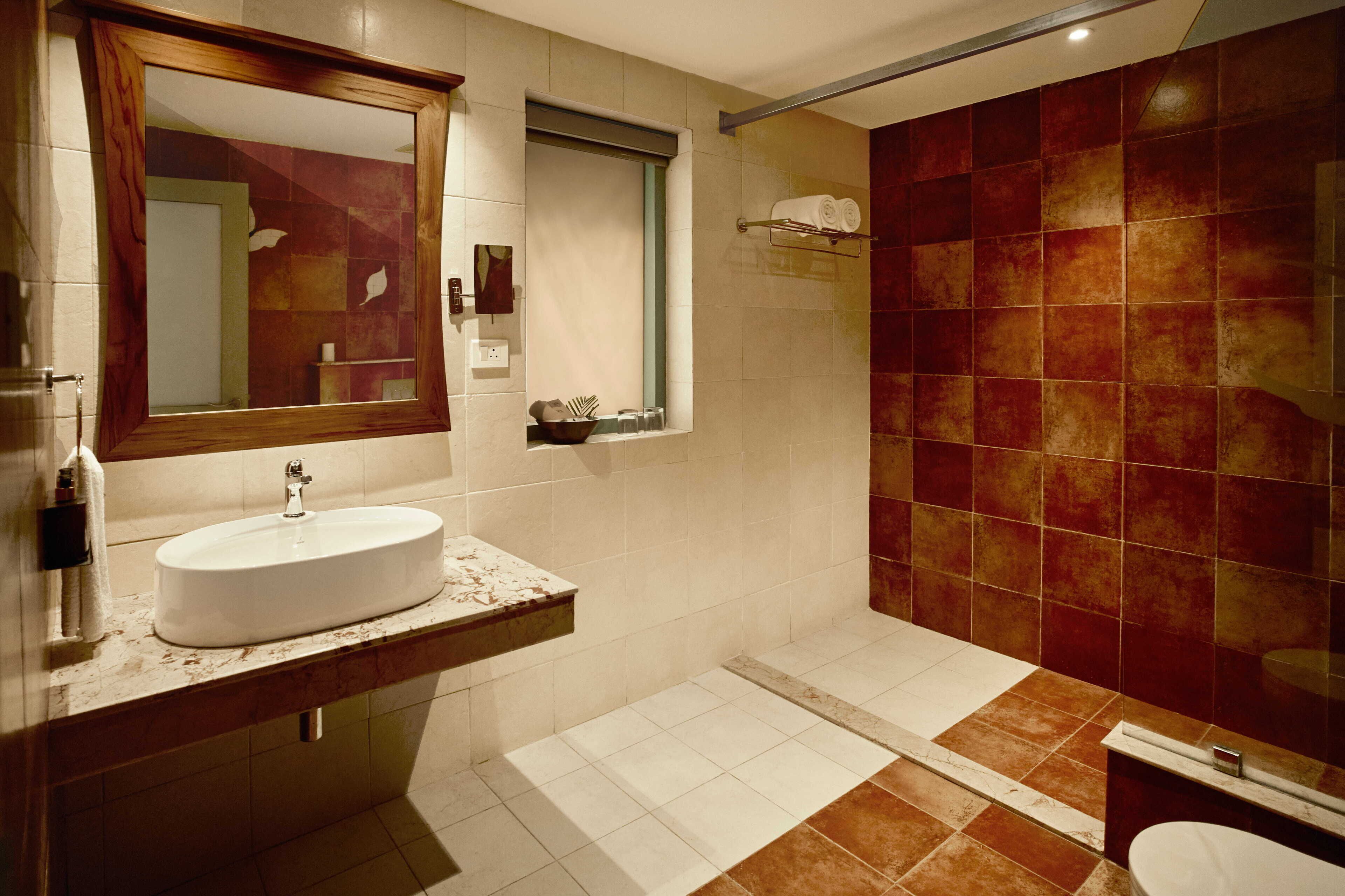 Un baño moderno con un espejo grande, un lavabo blanco y una zona de ducha con azulejos rojos.