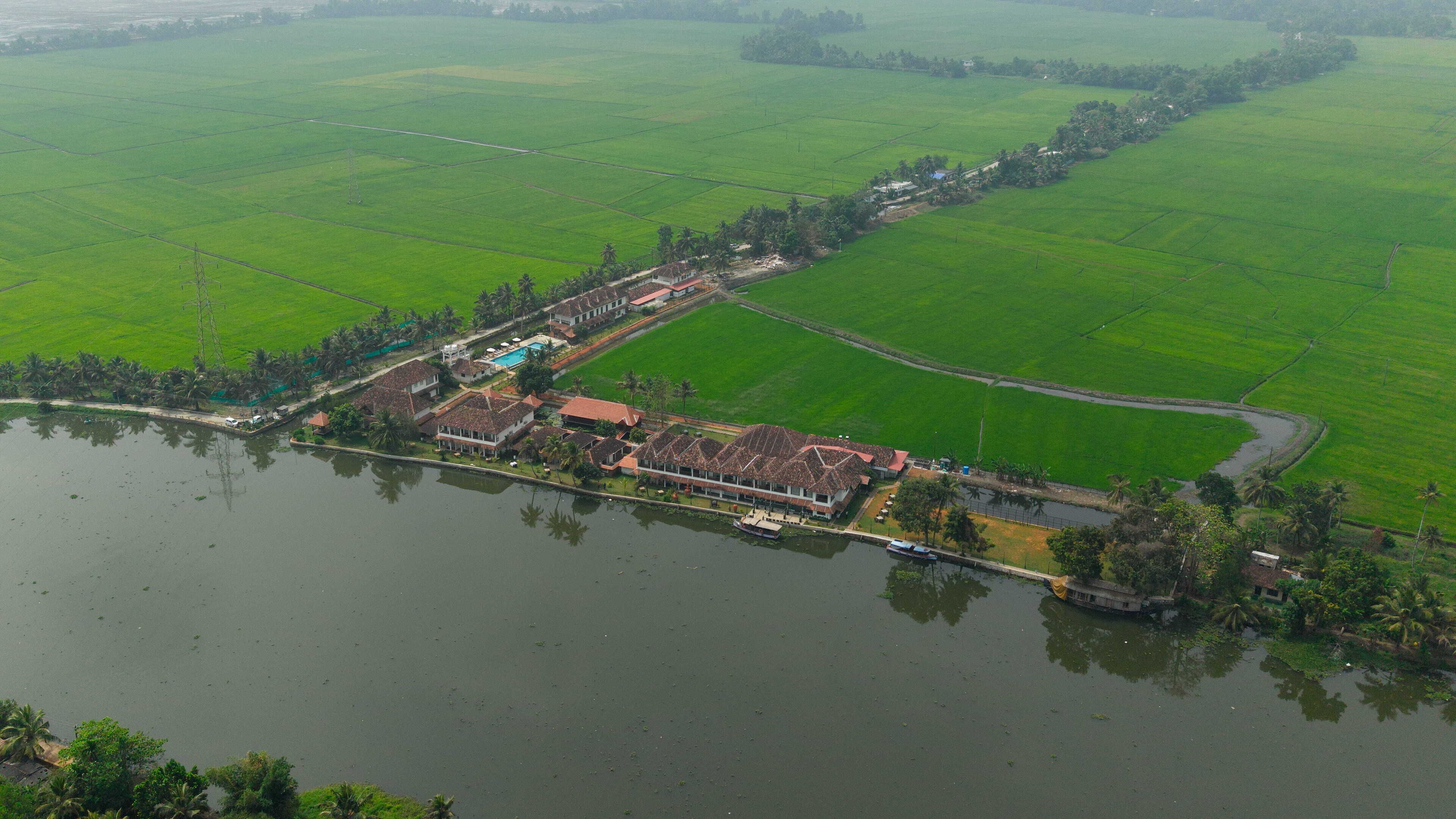 An aerial view of a coastal property with a large building complex, a swimming pool, and adjacent green fields.