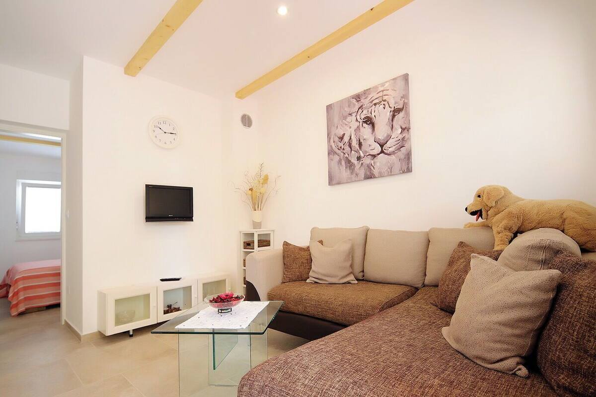 Un salon moderne avec un canapé beige, une table basse en verre, un téléviseur à écran plat, un tableau représentant un tigre et un jouet pour chien en peluche.