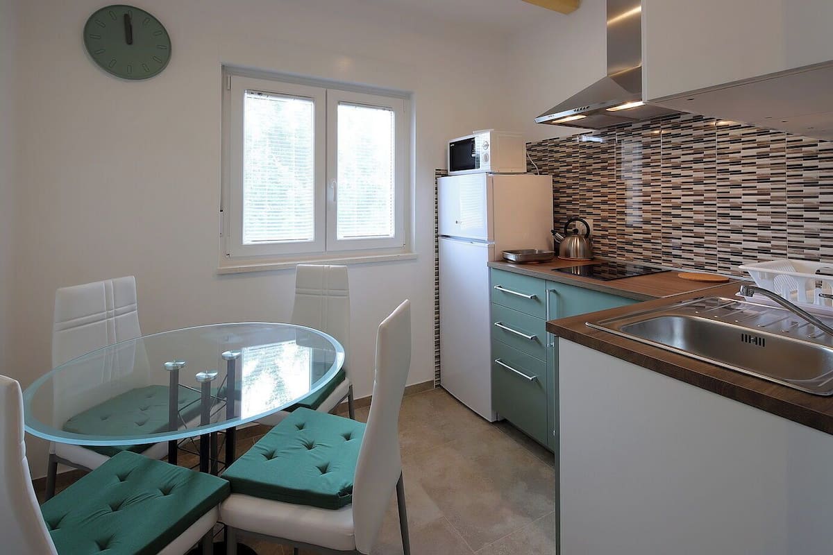 Une cuisine compacte avec une table ronde en verre, des chaises blanches, un four à micro-ondes, une bouilloire et un évier.