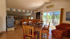 Amplia sala de estar con una mesa de comedor, sillas y un sofá rojo. Se ve una cocina al fondo, y hay un balcón con vistas al exterior.