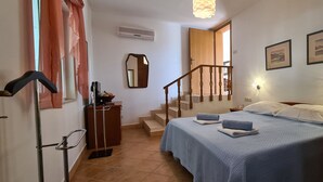 Un dormitorio con cama, mesita de noche, luz empotrada en la pared y una escalera que lleva a otra habitación.
