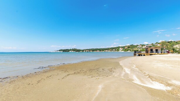 A beach with clear blue water, sandy shore, and a building with a lifeguard tower on the right. - Apartment Mario (Lopar)