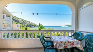 A balcony with a table and chairs, overlooking a coastal view. - Apartment Mario (Lopar)