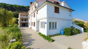 A two-story house with a balcony, a paved driveway, and a garden area. - Apartment Mario (Lopar)